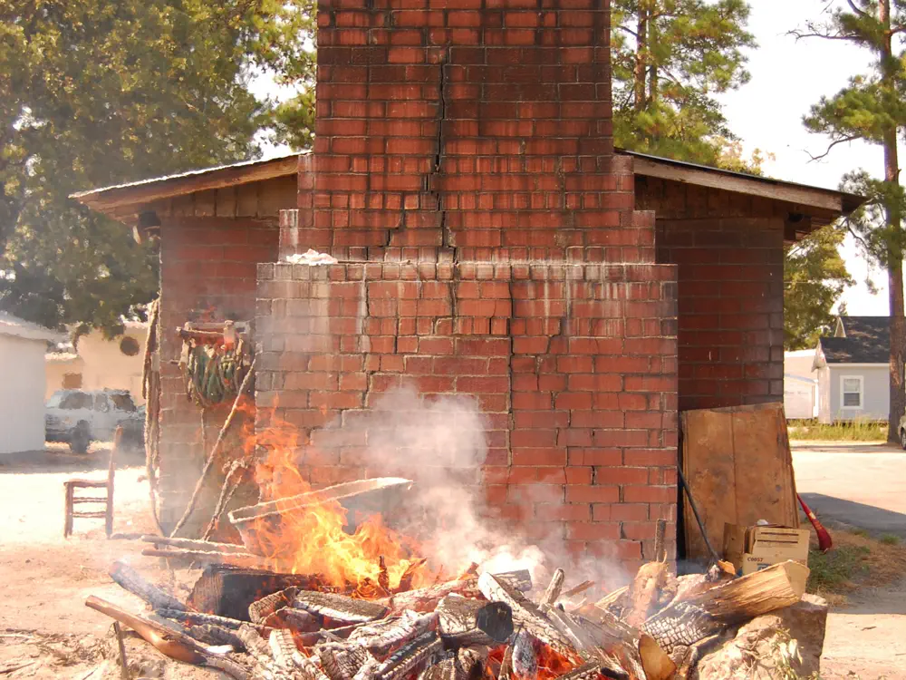 A hardwood fire burning down to coals beside a brick barbecue pit