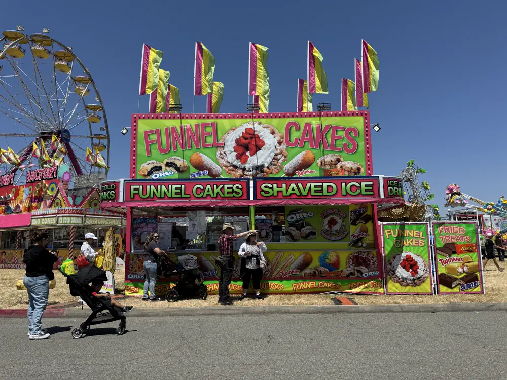 A funnel cake stand on the midway with a ferris wheel behind it
